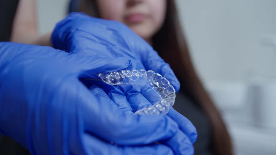 Alineador transparente sostenido con guantes clínicos frente a la paciente